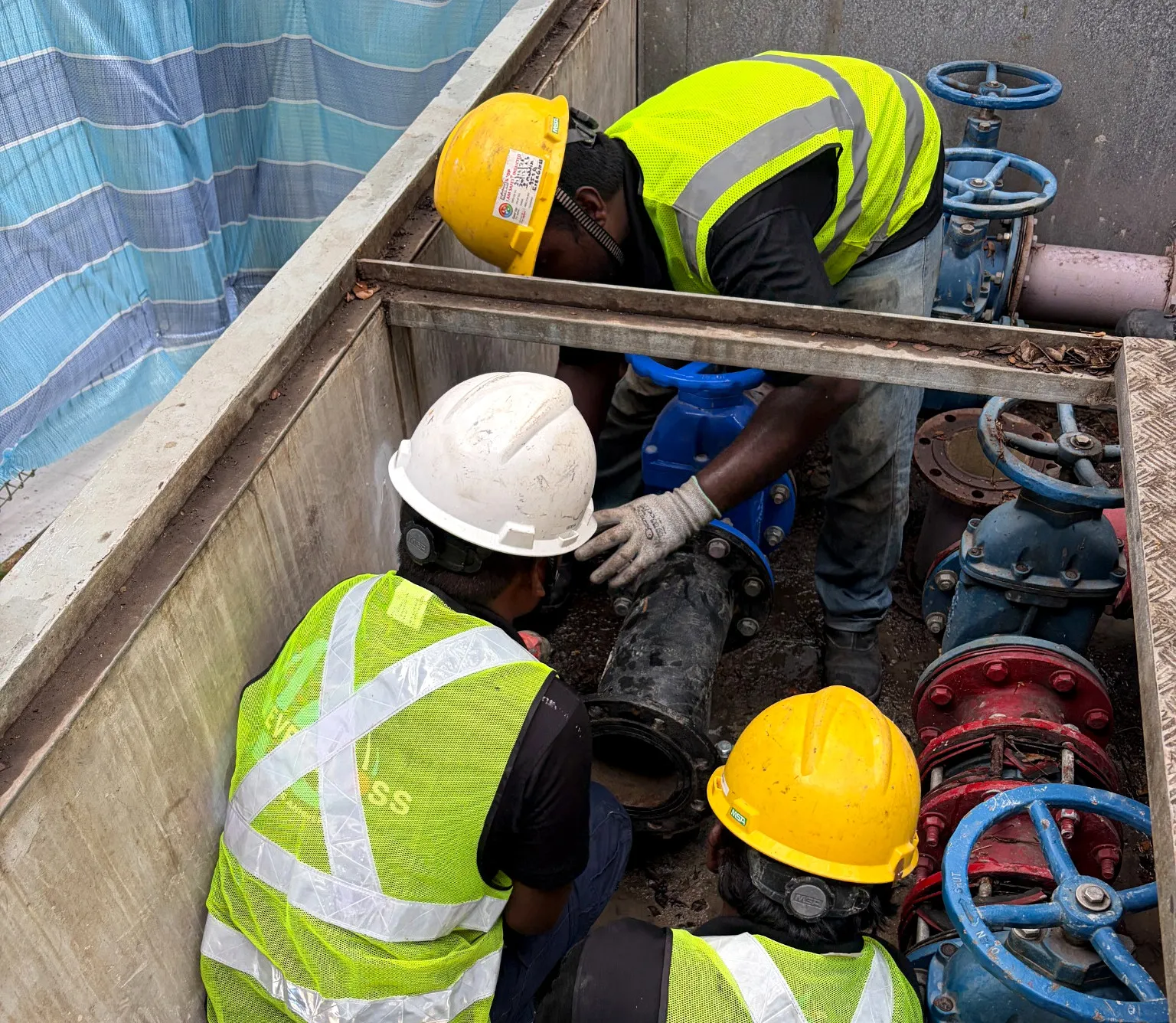Three Evergloss field workers handling a large pipeline in a water-main valve chamber